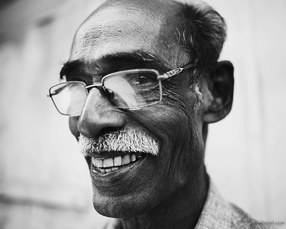 A 28mm wide angle black and white portrait of a bespectacled smiling man from Trivandrum, Kerala, India