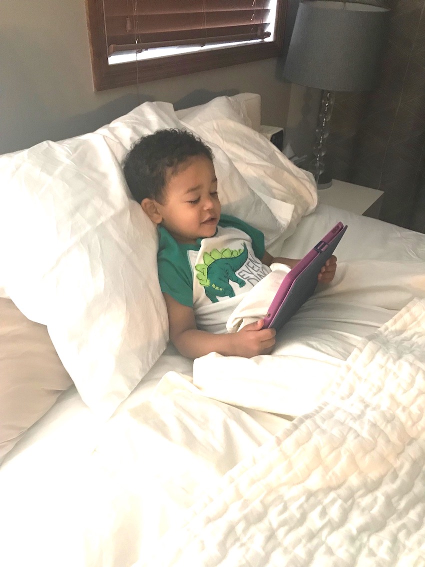 Photo of Elijah in bed watching the story of The Three Little Wolves and the Big Bad Pig on an iPad.